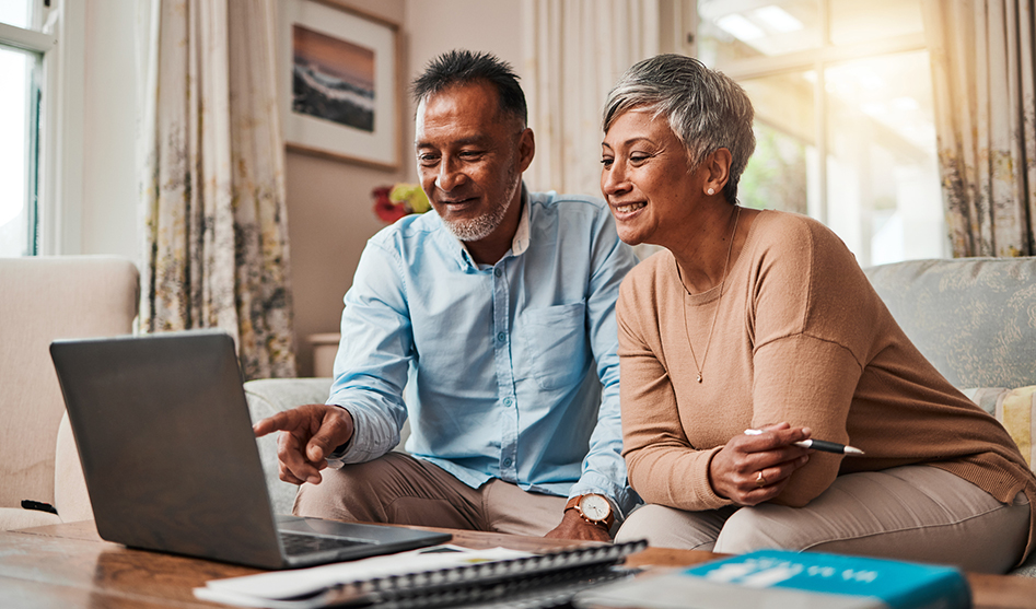 A couple sitting in front of a laptop reading.