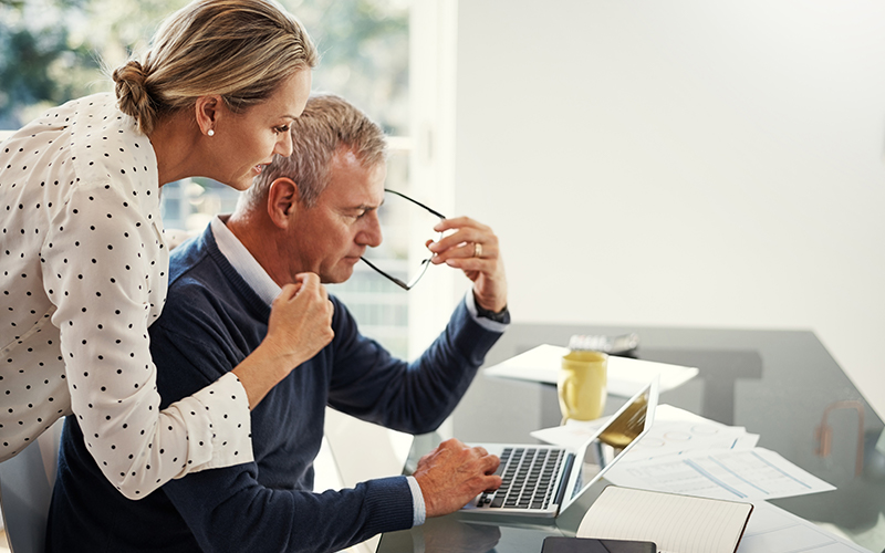 A retiree couple sitting in front of a computer talking